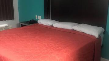 Un dormitorio con cama, mesita de noche y teléfono fijo en la pared.