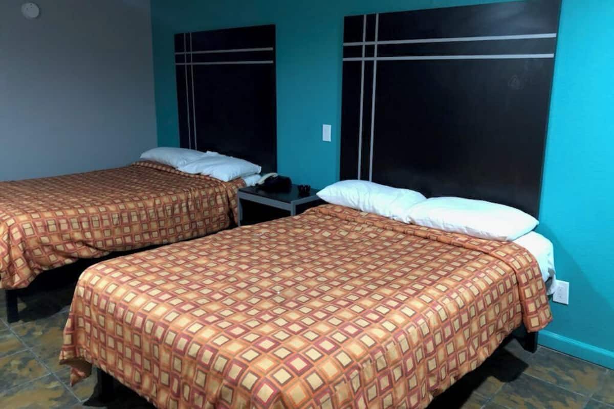 A room with two beds, each with a patterned bedspread and white pillows. The walls are painted teal, and there is a black headboard with a grid design.