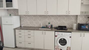 A compact kitchen with white cabinets, a built-in washing machine, and a microwave on the countertop.