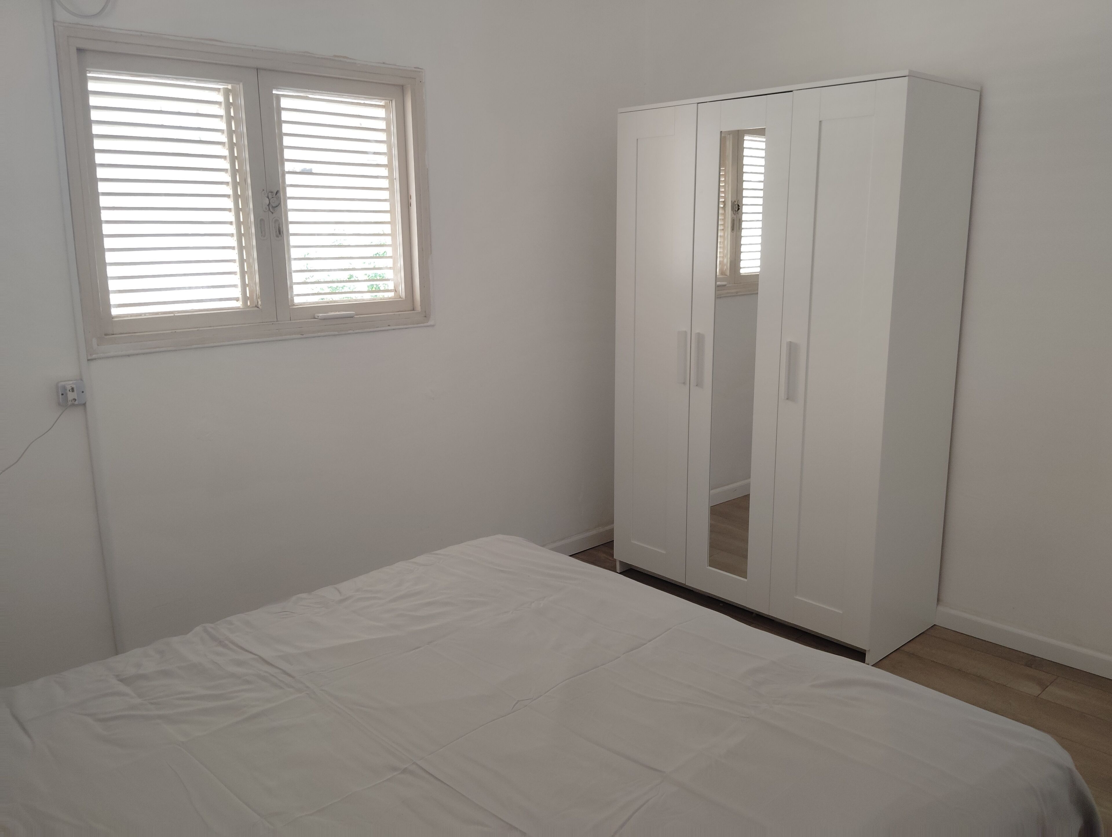 A bedroom with a single bed, a wardrobe, and a window with blinds.