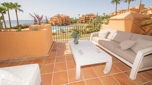 A balcony with a white sofa, a white coffee table, and a small potted plant. There is a pool visible in the background. - Los Granados de la Duquesa 1111 (Manilva)