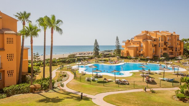 A resort with a central swimming pool, palm trees, and a view of the beach. - Los Granados de la Duquesa 1111 (Manilva)