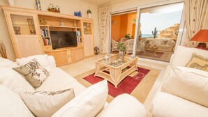 A living room with a TV, white sofas, a coffee table, and a view of the sea through a glass door. - Los Granados de la Duquesa 1111 (Manilva)