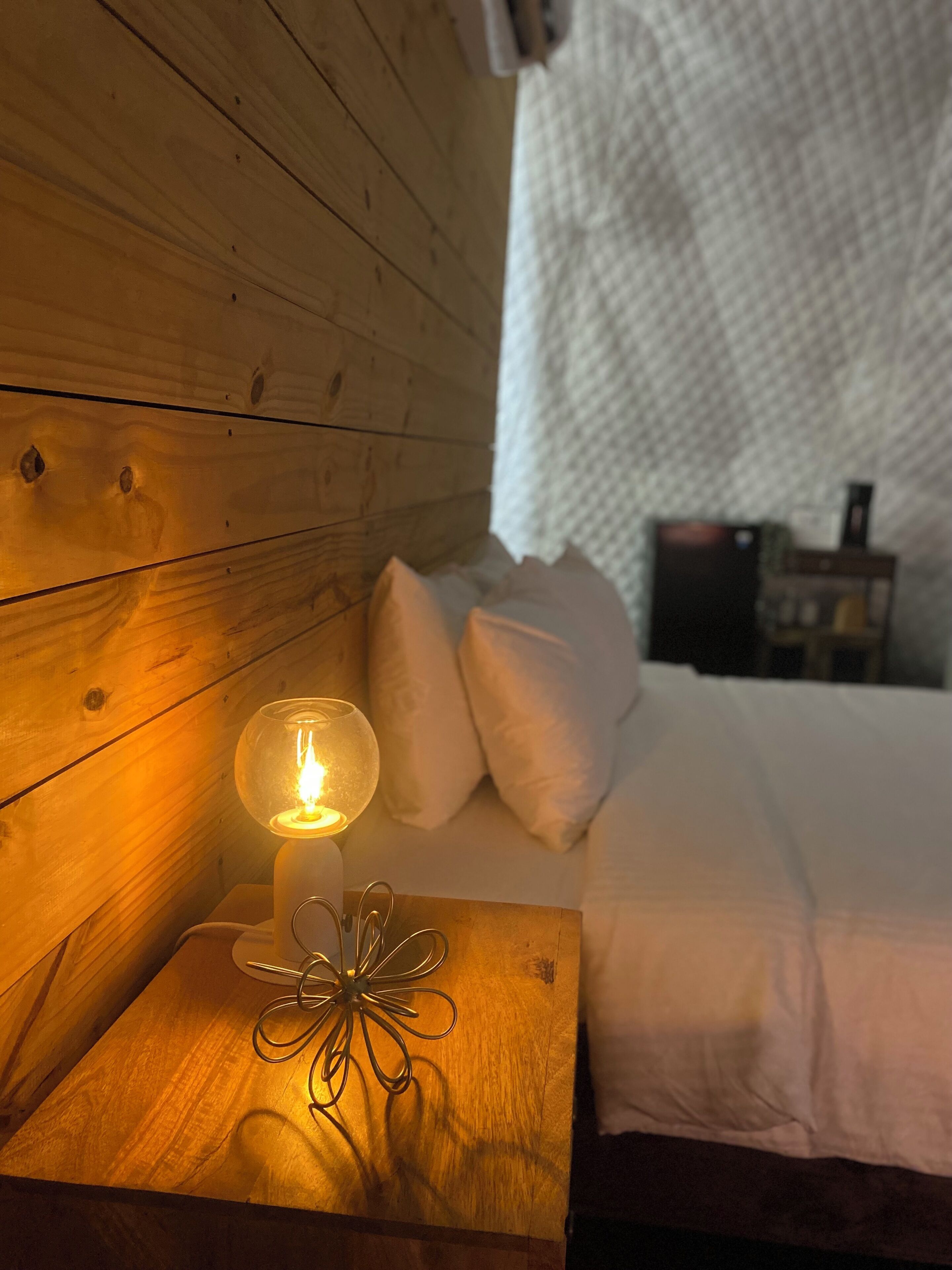 Cabecera de madera, lámpara de noche y cama con ropa blanca.