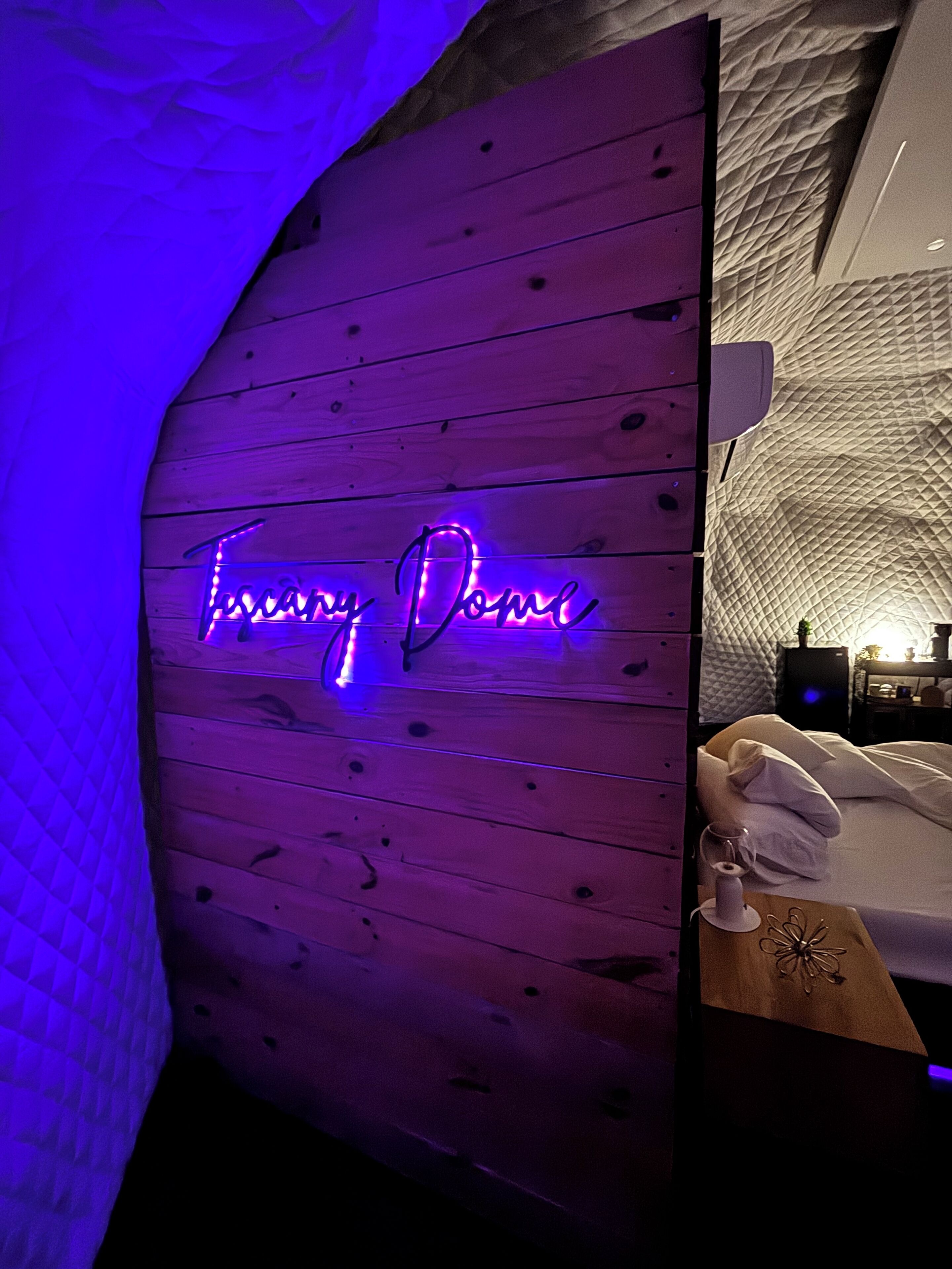 Una habitación con pared de paneles de madera y un letrero de neón que dice "Tuscany Dome".