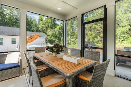 A covered patio with wicker furniture, a wooden table, and a flower vase.