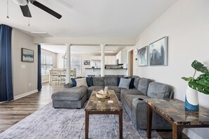 Una sala de estar moderna con un sofá seccional, una mesa de centro y un área de comedor al fondo.