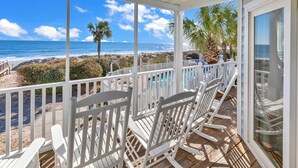 Eine überdachte Terrasse mit weißen Stühlen mit Blick auf einen Strand und das Meer.