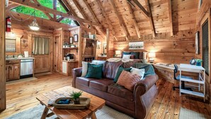 A cozy cabin interior with a wooden ceiling, a dining area, a sofa with cushions, a small table, and a kitchen area. - Romantic private cabin near Pigeon Forge - Hot Tub, Fireplace, Views!!! (Pigeon Forge)