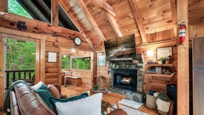 A cozy cabin interior with a wooden ceiling, a stone fireplace, a leather couch, and a dining area. - Romantic private cabin near Pigeon Forge - Hot Tub, Fireplace, Views!!! (Pigeon Forge)