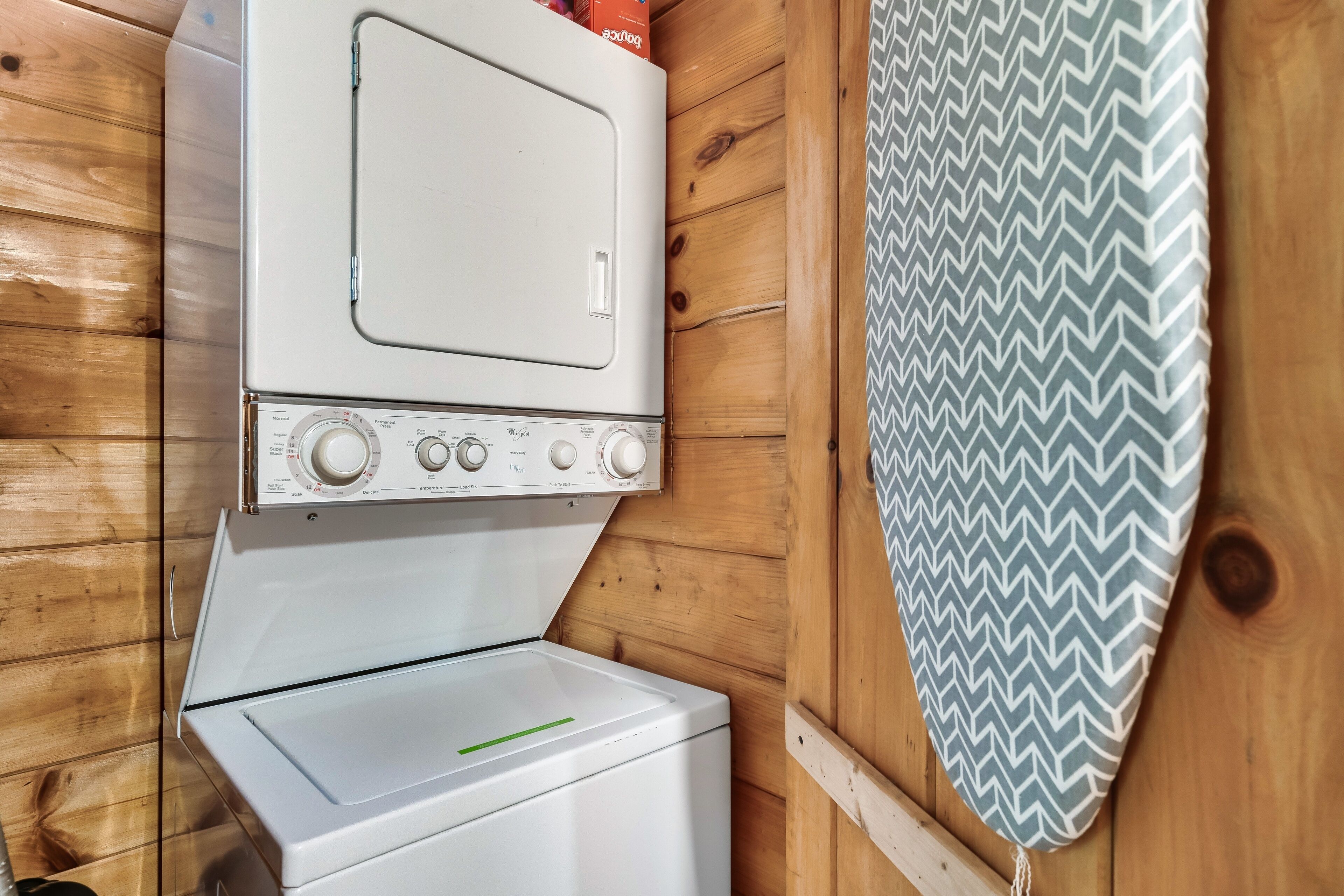 A compact laundry area with a stacked washer and dryer, wooden walls, and a patterned rug.