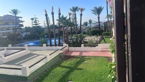 Un espace piscine avec une eau d’un bleu limpide, entouré de palmiers et d’une pelouse bien entretenue.