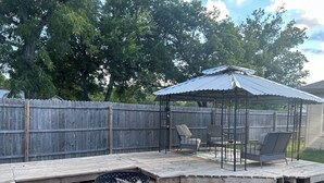 A backyard with a wooden deck, a fire pit, and a covered seating area.