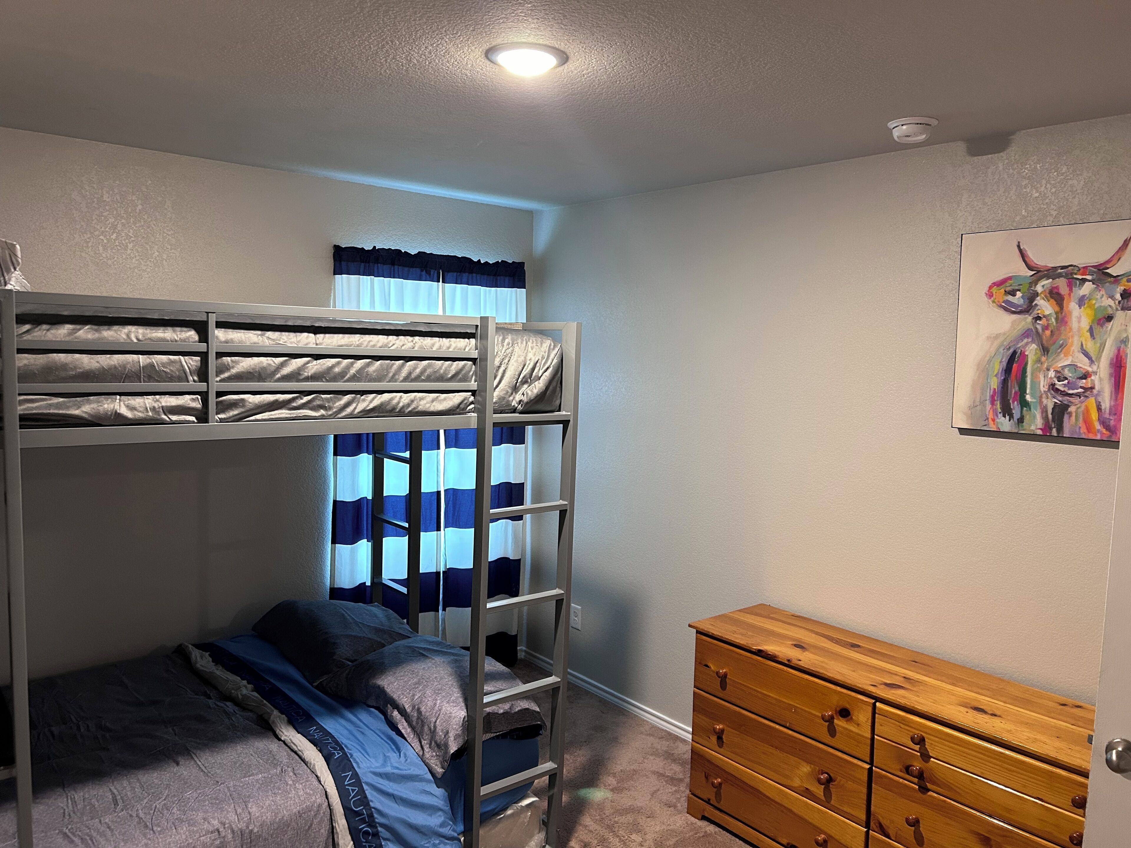 A bunk bed with a ladder, a dresser, and a painting on the wall.