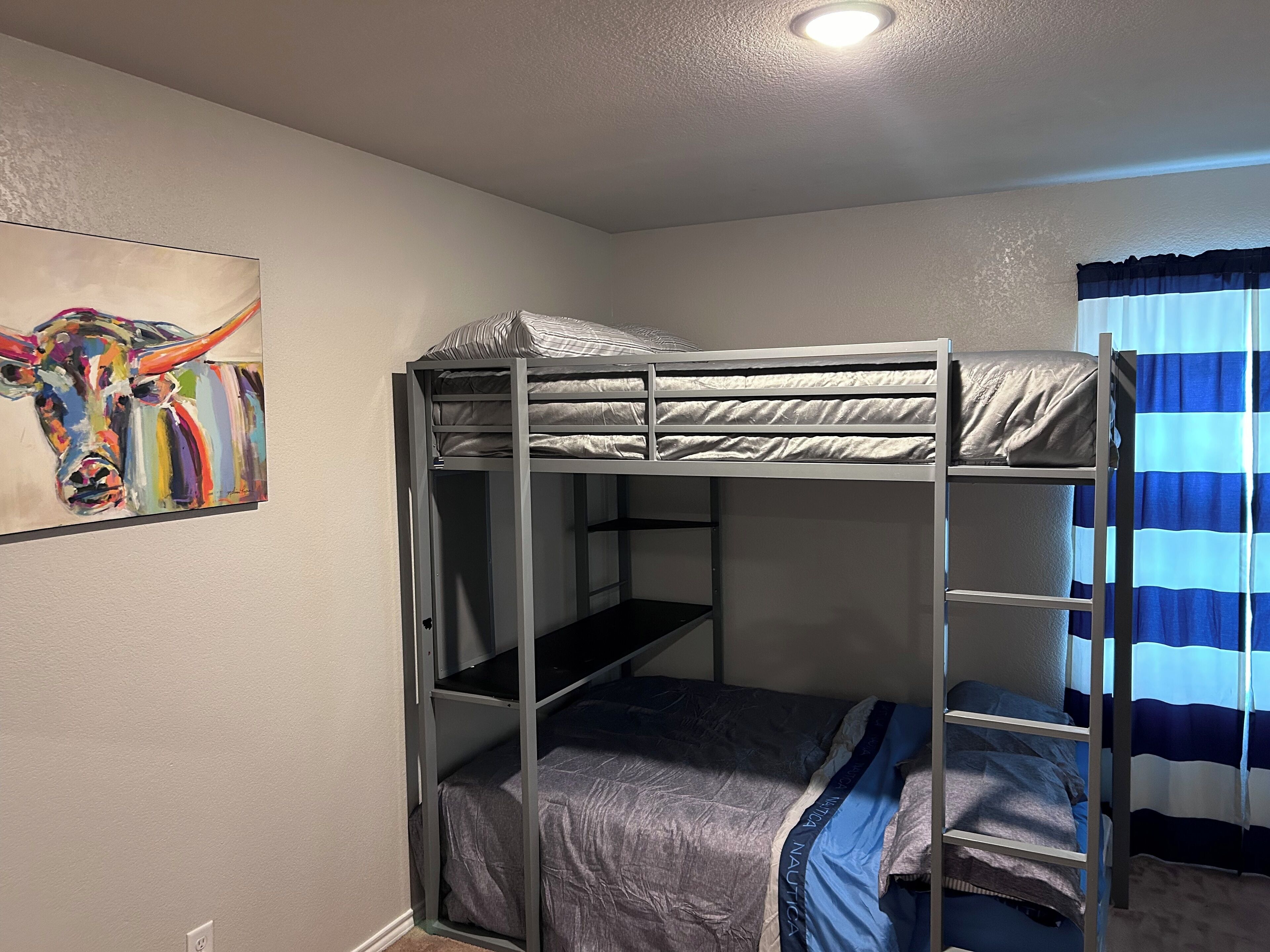 A bunk bed room with a ceiling light, a painting on the wall, and a striped curtain.