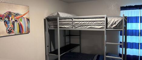 A bunk bed room with a ceiling light, a painting on the wall, and a striped curtain.
