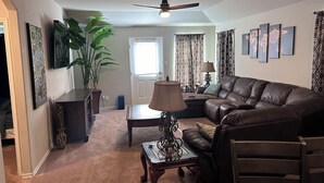 A living room with a brown leather sofa, a coffee table, a lamp, a potted plant, and a ceiling fan.