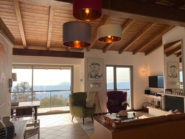 Un salon spacieux avec balcon, des poutres apparentes en bois au plafond et une grande fenêtre offrant une vue sur les montagnes.