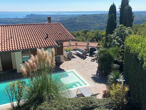 Une maison avec un toit en tuiles, une piscine et un patio aménagé avec du mobilier d’extérieur.