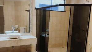 Ένα σύγχρονο μπάνιο με ένα διαχωριστικό ντους από γυαλί, έναν μεγάλο καθρέφτη και μια λευκή τουαλέτα.