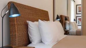 Ein Bett mit weißen Kissen, einem gewobenen Kopfteil und einer Nachttischlampe.
