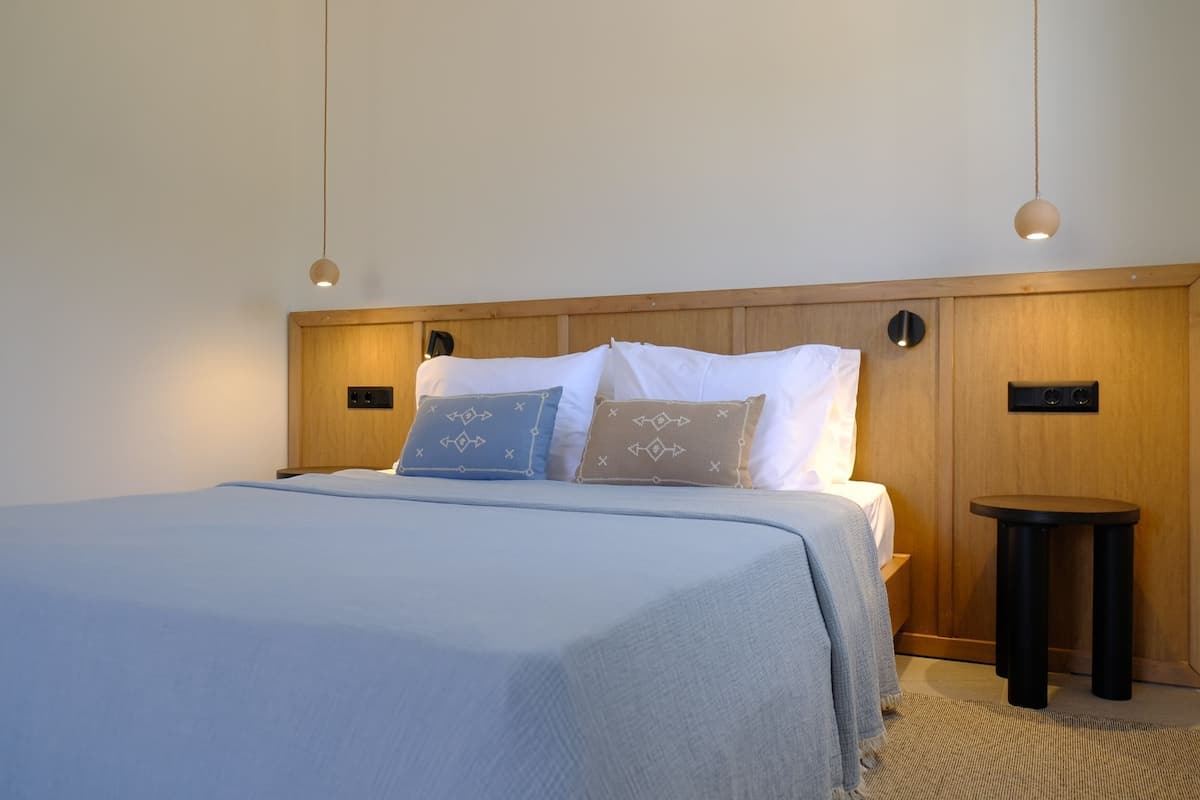 Un lit bien fait, recouvert d’une courtepointe bleu clair, avec deux oreillers aux motifs géométriques, et une petite table ronde placée à côté du lit.