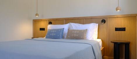 A neatly made bed with a light blue bedspread, two pillows with geometric patterns, and a small round table beside the bed.