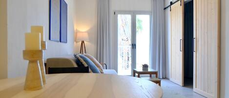 A modern room with a bed, a dining table with candles, a lamp, and a sliding door to a balcony.