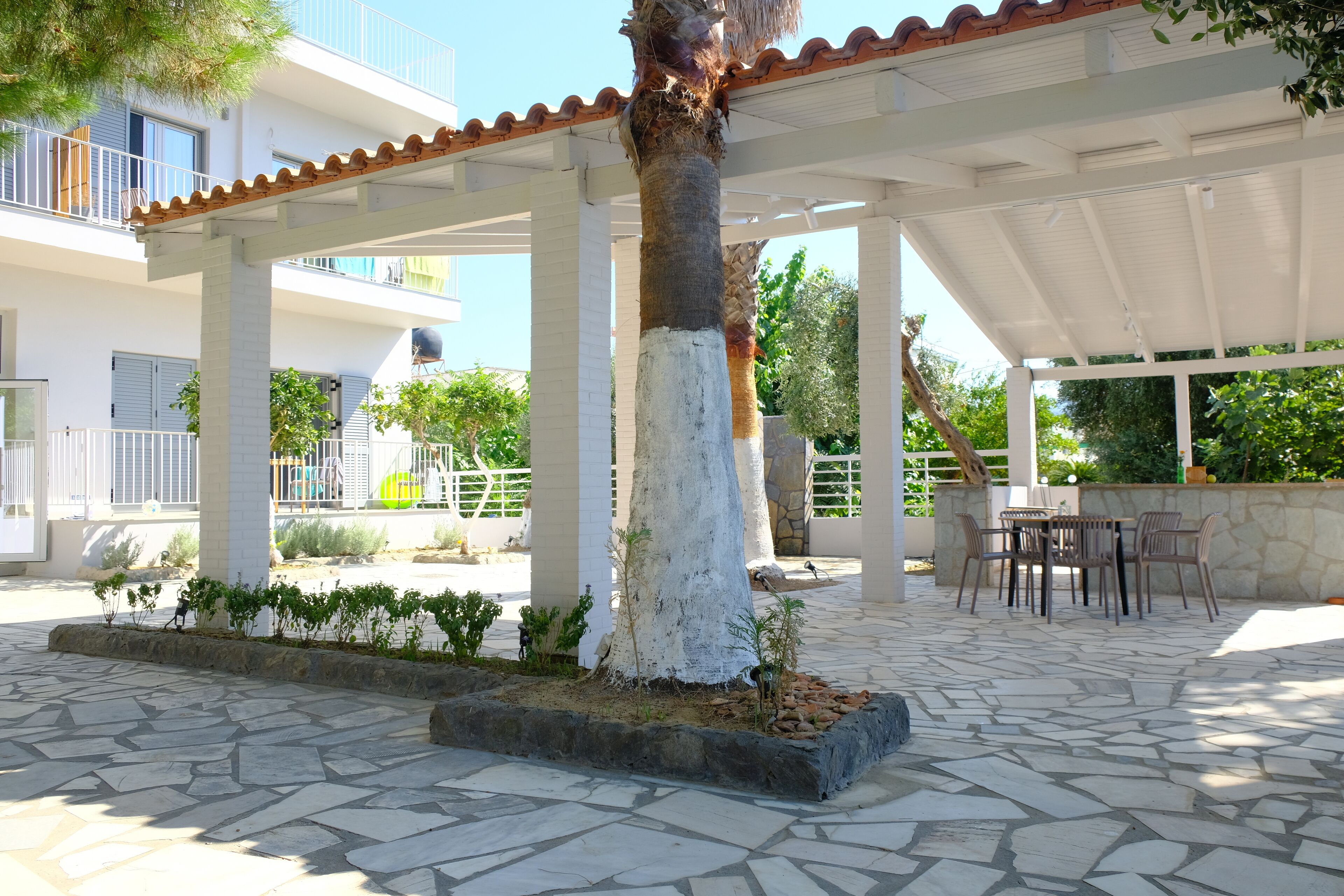 Un espacio al aire libre cubierto con suelo de piedra, una palmera y una zona de estar con sillas y una mesa.