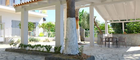 Un espacio al aire libre cubierto con suelo de piedra, una palmera y una zona de estar con sillas y una mesa.