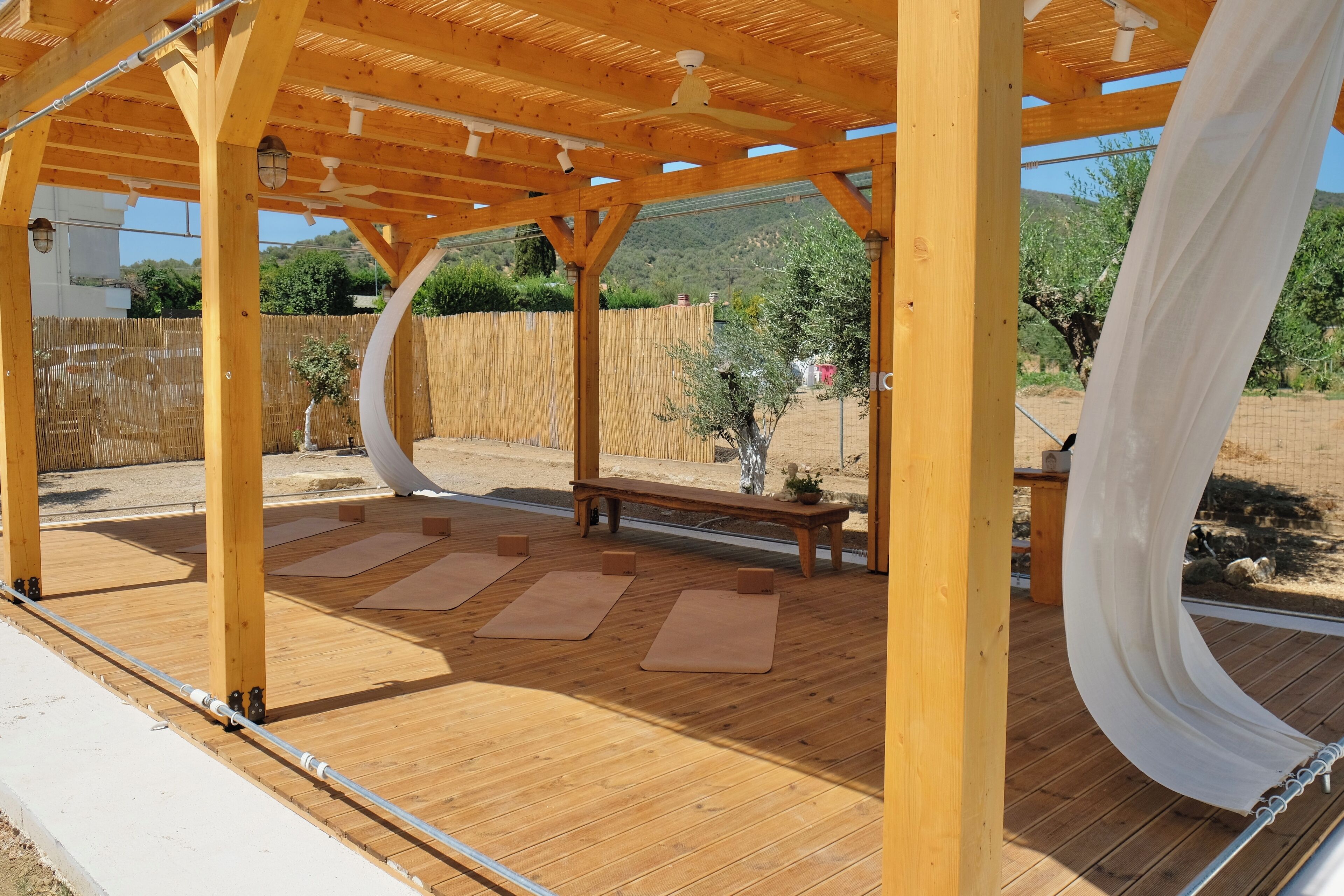 Una terraza de madera con una pérgola, colchonetas de ejercicio y un banco.
