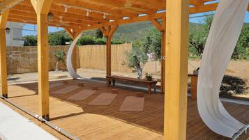 Una terraza de madera con una pérgola, colchonetas de ejercicio y un banco.