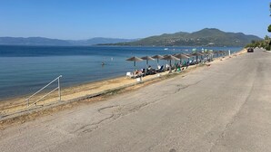Una playa con sombrillas y sillas reclinables, una carretera y vistas al mar y a las colinas.