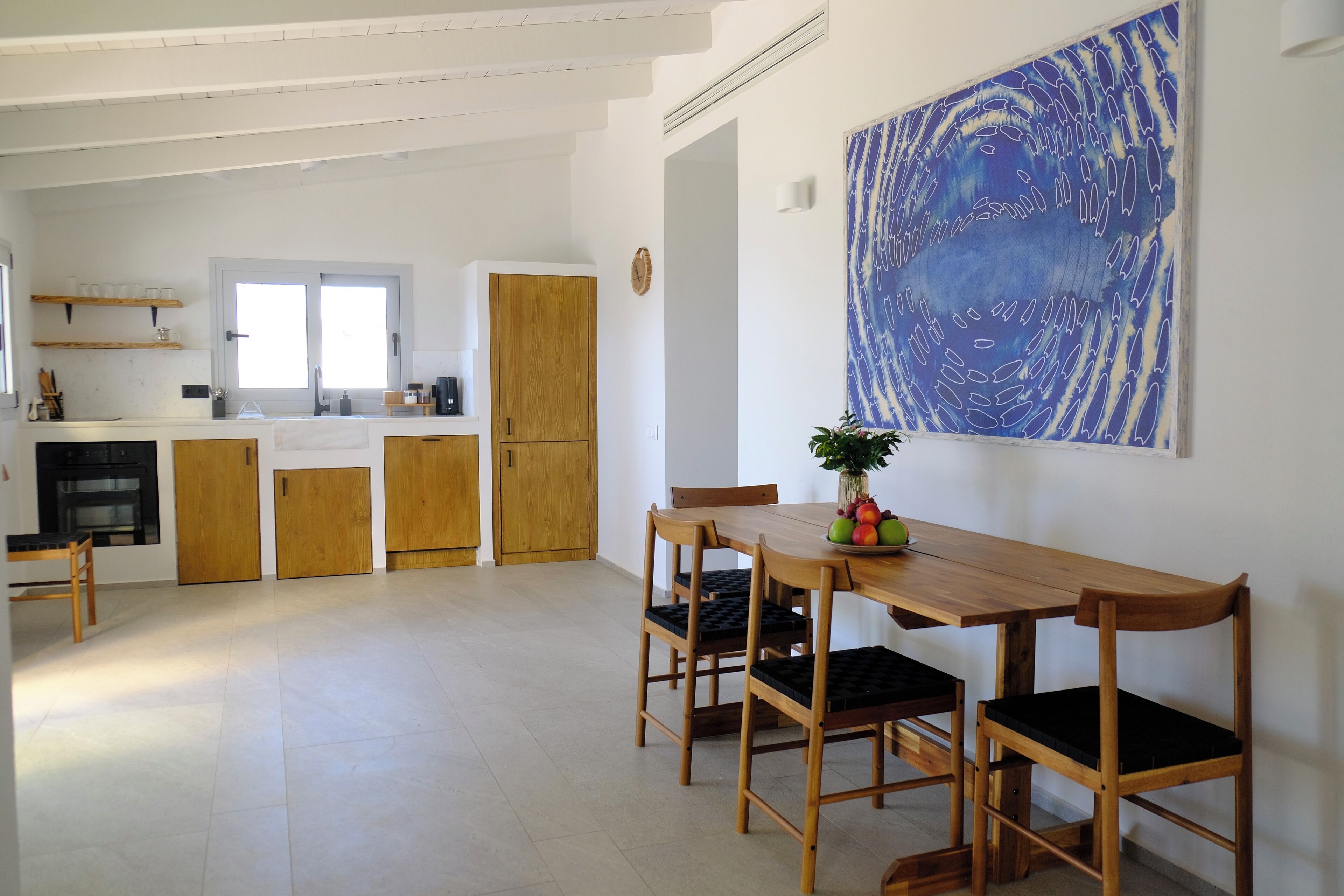 Eine geräumige Küche mit Holzschränken, ein Essbereich mit einem Holztisch und Stühlen sowie ein großes abstraktes Gemälde an der Wand.
