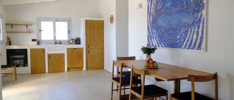 A spacious kitchen with wooden cabinets, a dining area with a wooden table and chairs, and a large abstract painting on the wall.