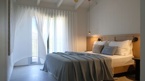 Un dormitorio con cama, mesita de noche, cabecero de madera y ventana con cortinas de encaje.