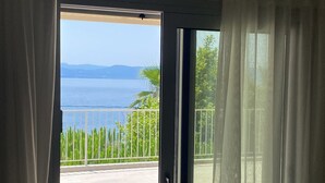 Una habitación con puerta corrediza de vidrio que da a un balcón con vista al mar y las montañas.