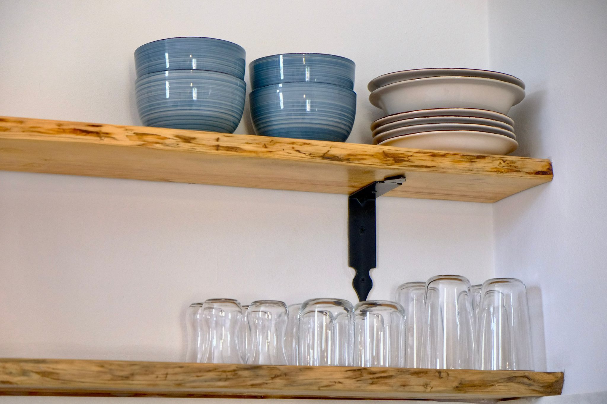 A wooden shelf with stacked plates and clear glassware.