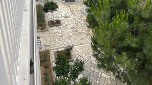 Un balcón con un patio de baldosas de piedra, una palmera y vistas a una playa y montañas.