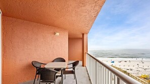 Enjoy breathtaking views of the beach from this balcony, featuring a table and two chairs.