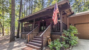 A cabin with a porch, a flag, and a bear statue.