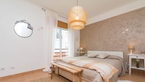 Un dormitorio con cama, mesitas de noche, lámpara colgante, espejo y vistas al exterior.