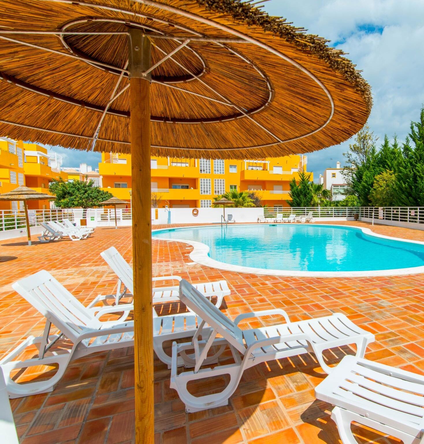 Un espace piscine avec des chaises longues blanches et un parasol en chaume.
