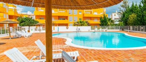 A swimming pool area with white lounge chairs and a thatched umbrella.