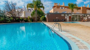 Una piscina azul cristalina con una escalera metálica, rodeada por una terraza de madera y palmeras.