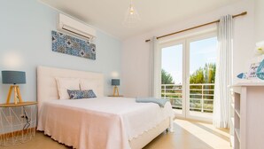 Un dormitorio con una cama grande, dos mesitas de noche, una lámpara de techo, una ventana con cortinas y vistas a zonas verdes.