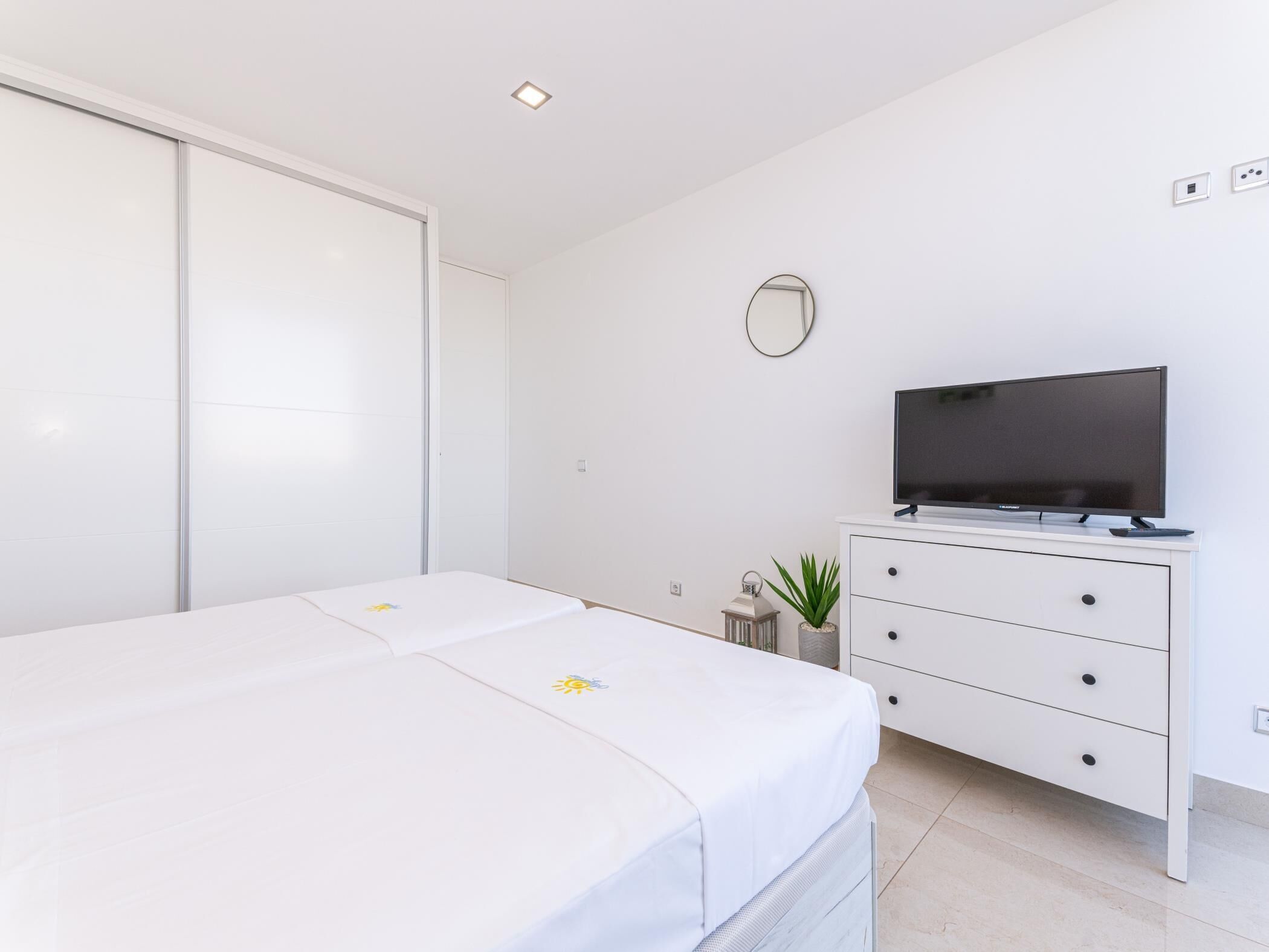 Une chambre moderne avec un lit, un téléviseur posé sur une commode et un placard à portes coulissantes.
