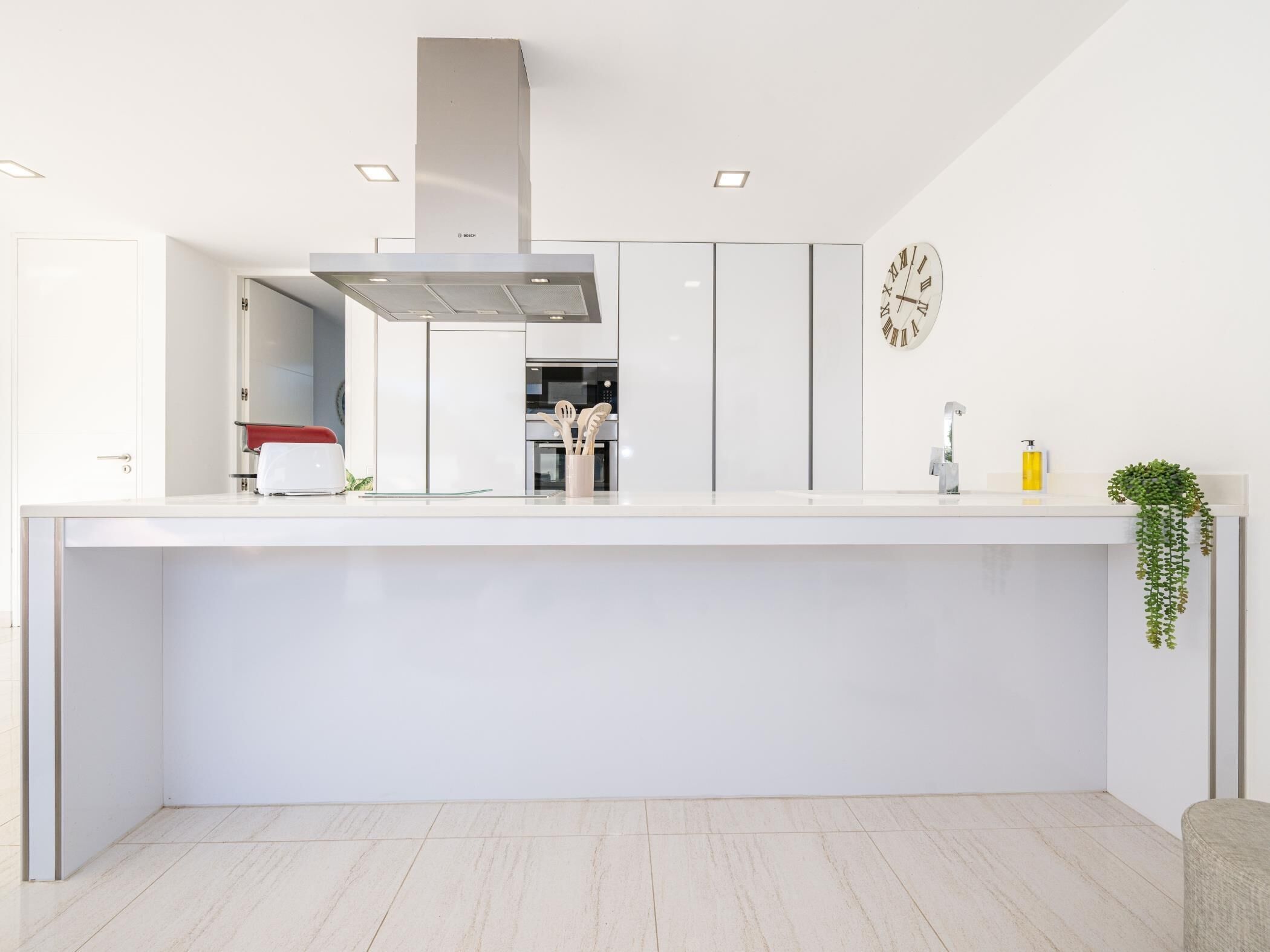 Una cocina moderna con armarios blancos, una campana de acero inoxidable y un reloj de pared.