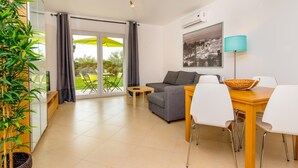 Una sala de estar moderna con sofá, mesa de comedor, sillas y un balcón con mobiliario exterior.