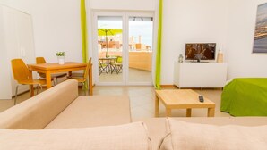 A living room with a sofa, a dining table with chairs, a TV, and a balcony with a table and chairs.